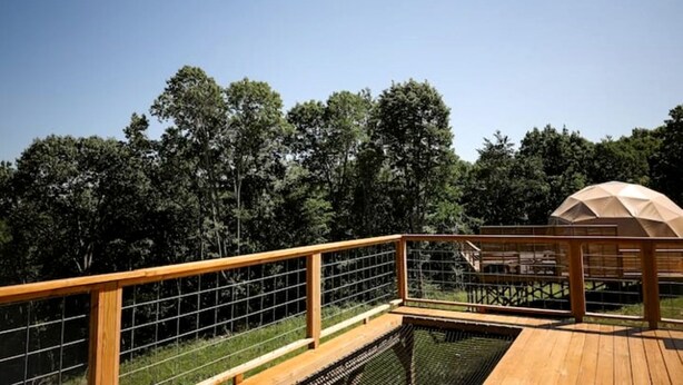 A wooden deck with a metal railing, a covered seating area, and a view of dense trees.