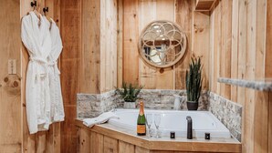 Une salle de bain rustique, avec des murs en bois, comprenant une baignoire, un peignoir suspendu à un porte-manteau, une bouteille de champagne et une plante en pot.