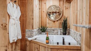 Une salle de bain rustique, avec des murs en bois, comprenant une baignoire, un peignoir suspendu à un porte-manteau, une bouteille de champagne et une plante en pot.