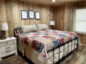 A wooden-paneled bedroom with a bed, bedside tables, and framed pictures on the wall.
