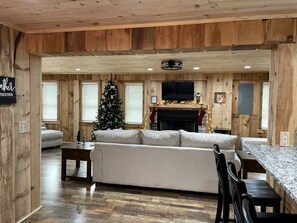 A cozy cabin interior with a wooden interior, a sofa, a dining table, a fireplace, and a Christmas tree.