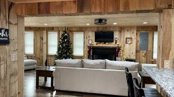 A cozy cabin interior with a wooden interior, a sofa, a dining table, a fireplace, and a Christmas tree.