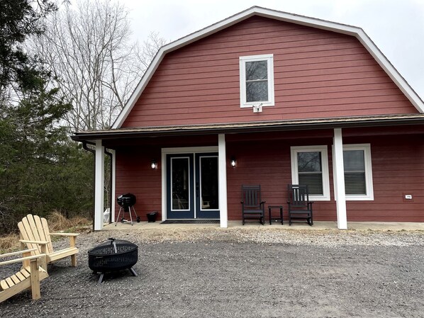 Un bâtiment rouge avec un porche, deux chaises, un barbecue et un foyer.