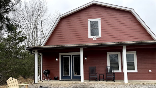 Un bâtiment rouge avec un porche, deux chaises, un barbecue et un foyer.