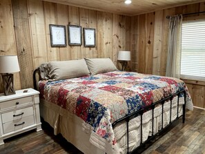 A wooden-paneled bedroom with a bed, bedside tables, and framed pictures on the wall.