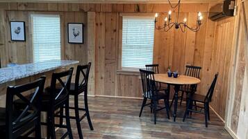 A wooden-paneled room with a kitchen area, dining table, chairs, and framed pictures on the walls.