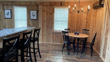 A wooden-paneled room with a kitchen area, dining table, chairs, and framed pictures on the walls.