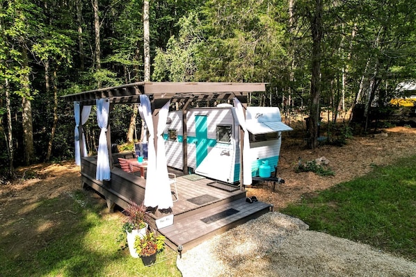 A mobile home with a porch and a small deck, surrounded by trees. - Vintage Camper Rental in Franklin for Couples Getaway in the Mountains in North Carolina (Franklin)