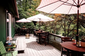 A wooden deck with outdoor furniture, including tables and chairs, and umbrellas providing shade. - Vintage Camper Rental in Franklin for Couples Getaway in the Mountains in North Carolina (Franklin)