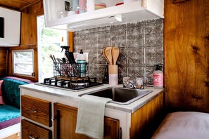 A compact kitchen with a gas stove, a sink, wooden cabinets, and a window with a view.