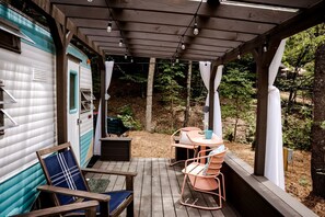 A covered porch with a table and chairs, a small deck, and a camper parked adjacent. - Charming Vintage Caravan Rental in Franklin, North Carolina for Mountain Glamping Escape (Franklin)