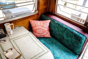 A cozy interior with a teal upholstered bench, a red patterned pillow, a white mug, and a clipboard on a table.