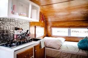 A compact RV interior with a kitchenette, a bed with pillows, and a window providing a view.