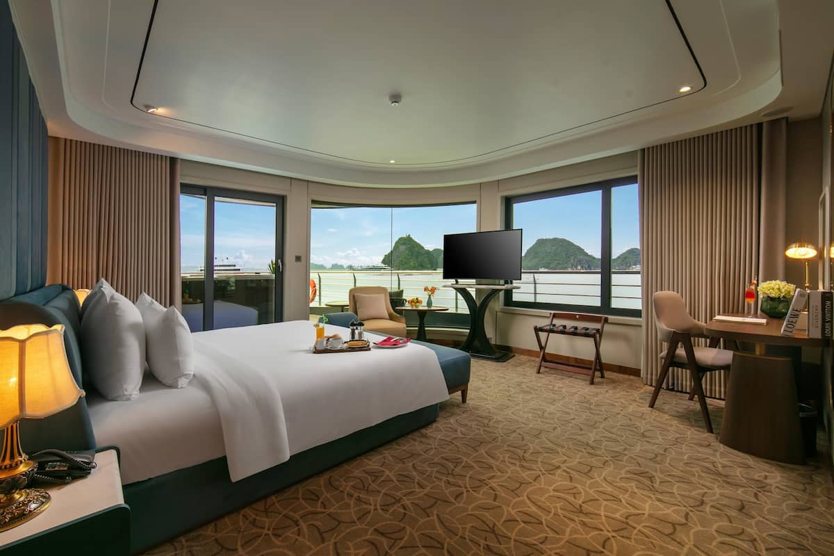 Ein Hotelzimmer mit einem großen Bett, einem Schreibtisch, einem Sessel, einem Fernseher und Blick auf die Berge.