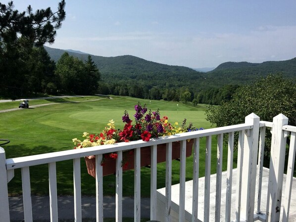 Blick auf einen Golfplatz mit weißem Zaun und Blumenkästen im Vordergrund.