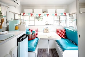 A compact RV interior with a kitchenette, a dining area, and a seating space with a table and chairs.