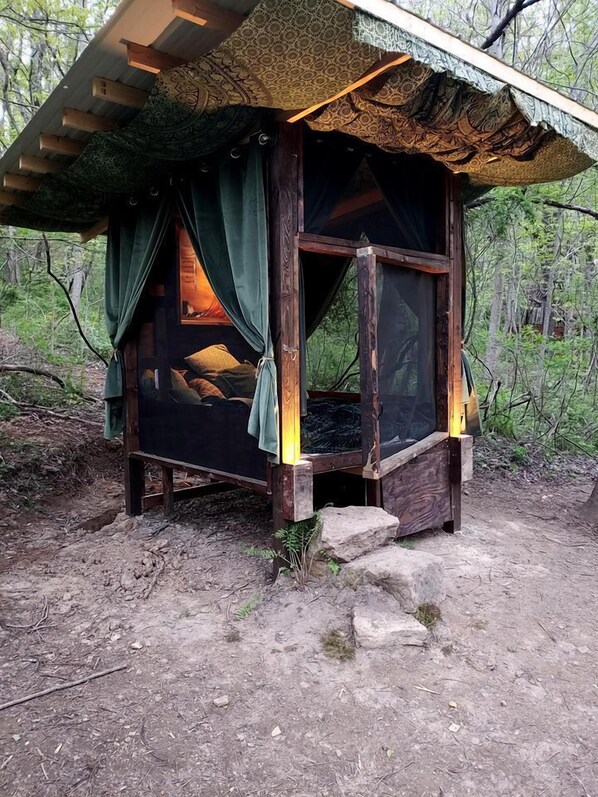 A rustic wooden cabin with a bed, curtains, and a window.