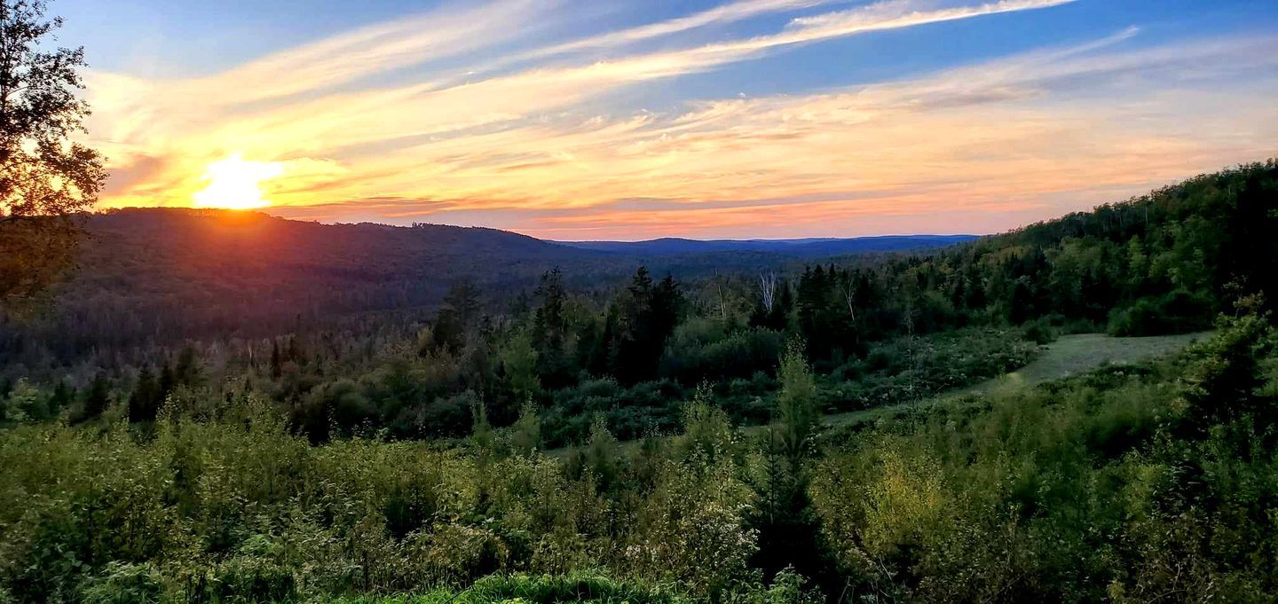 A natural landscape with a sunset, hills, and a path.
