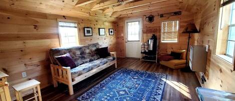 L’intérieur d’un chalet en bois, avec un canapé, un tapis, une lampe et un téléviseur.