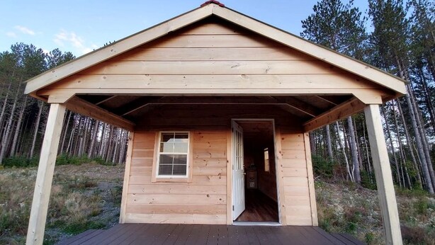 Eine Holzhütte mit überdachter Veranda, einem Fenster und einer Tür.