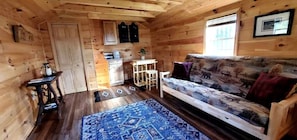 A wooden cabin interior with a sofa, a small table, a cabinet, and a window. - Off-Grid Cabin Nestled Among Nature with Lovely Landscape Views in Maine (Grand Isle)