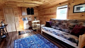 Ein Interieur einer Holzhütte mit einer Couch, einem kleinen Tisch, einem Schrank und einem Fenster.