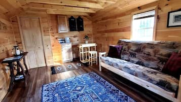 A wooden cabin interior with a sofa, a small table, a cabinet, and a window.
