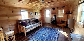 Ein Holzblockbau-Innenraum mit einer Couch, einem Teppich, einer Lampe und einem Fernseher.