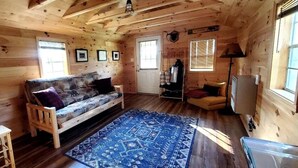 Ein Holzblockbau-Innenraum mit einer Couch, einem Teppich, einer Lampe und einem Fernseher.