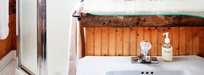 A bathroom with a wooden panel wall, a glass shower enclosure, a white sink with a soap dispenser, and a towel hanging on a rack. - Lovely Suite Rental for Two at Countryside Bed and Breakfast in Warren, Vermont (Warren)