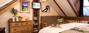 A bedroom with a lofted ceiling, a bed with a quilt, a wooden dresser, a lamp, a TV, and a poster of a skier. - Lovely Suite Rental for Two at Countryside Bed and Breakfast in Warren, Vermont (Warren)