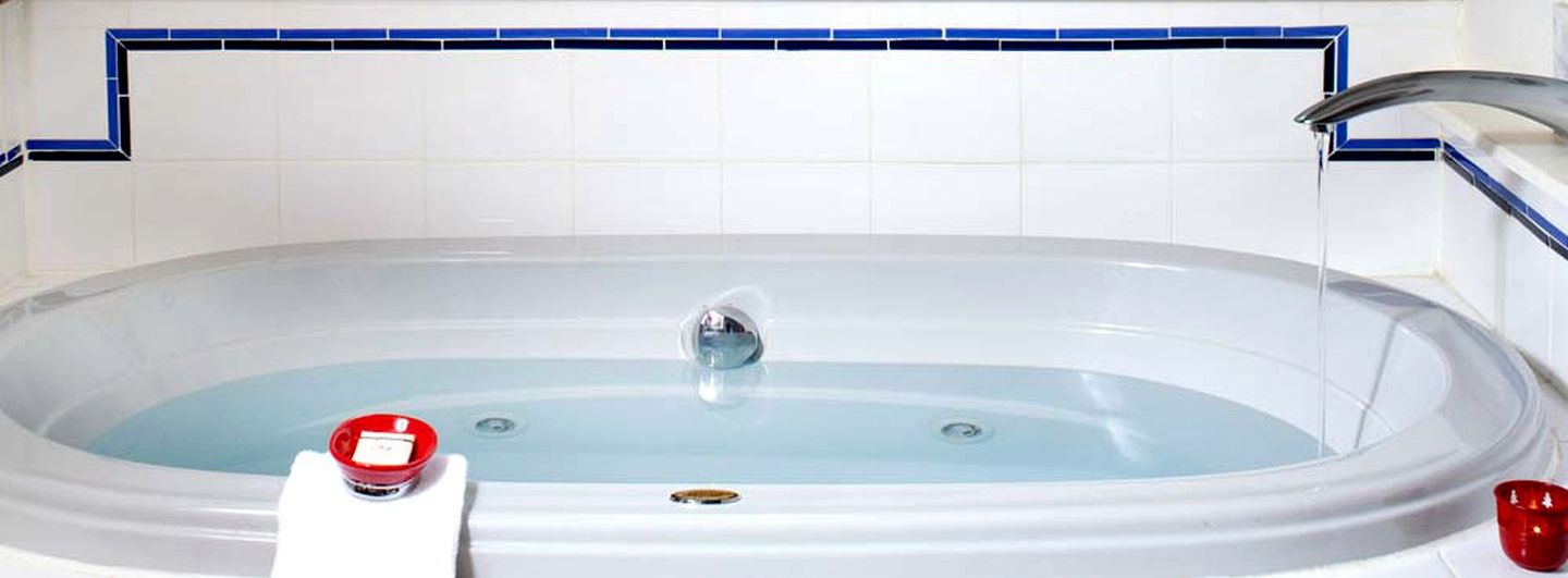 A bathtub with a faucet, a red object on the side, and a blue-tiled wall.