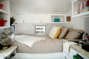 A bedroom with a bed, a fan, a window, and storage cabinets.