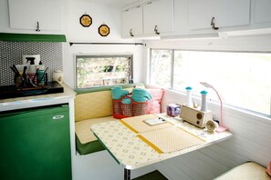 A compact kitchen with a green cabinet, a window with a view, a table with a yellow patterned tablecloth, and a radio.