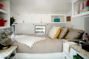 A bedroom with a bed, a fan, a window, and storage cabinets.