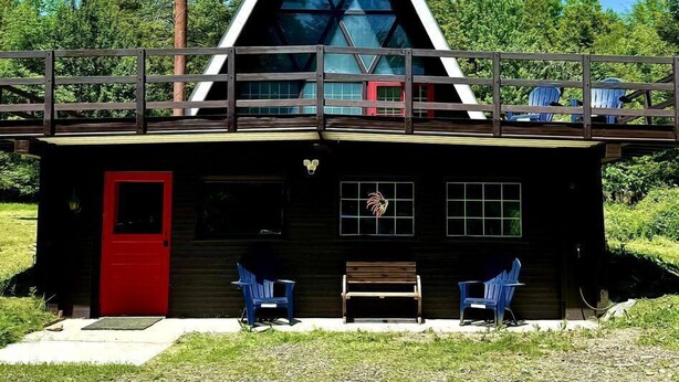 A cabin with a red door, a wooden deck, and two blue chairs.