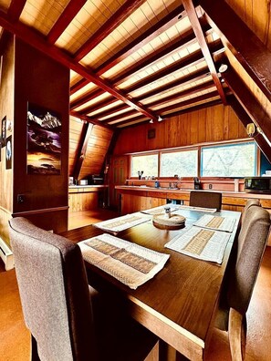 A wooden interior with a dining table set for four, a kitchen area, and large windows.