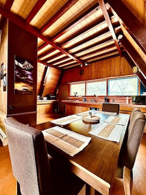 A wooden interior with a dining table set for four, a kitchen area, and large windows.