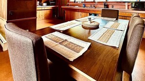 A wooden interior with a dining table set for four, a kitchen area, and large windows.