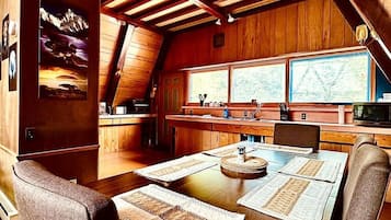 A wooden interior with a dining table set for four, a kitchen area, and large windows.