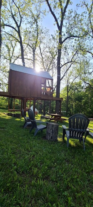 A wooden deck with a metal roof, surrounded by trees, and two Adirondack chairs.