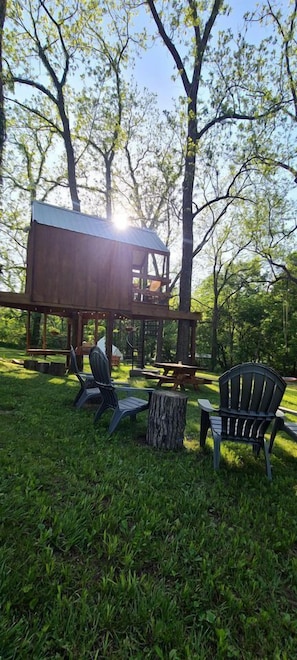A wooden deck with a metal roof, surrounded by trees, and two Adirondack chairs.