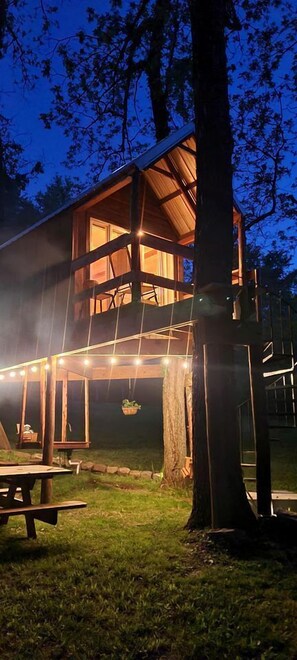 Une cabane en bois dotée d’un balcon, de guirlandes lumineuses et d’une table de pique-nique.