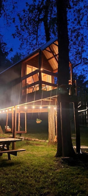 A wooden cabin with a balcony, string lights, and a picnic table.