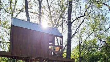 A wooden deck with a metal roof, surrounded by trees, and two Adirondack chairs.
