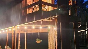 Une cabane en bois dotée d’un balcon, de guirlandes lumineuses et d’une table de pique-nique.