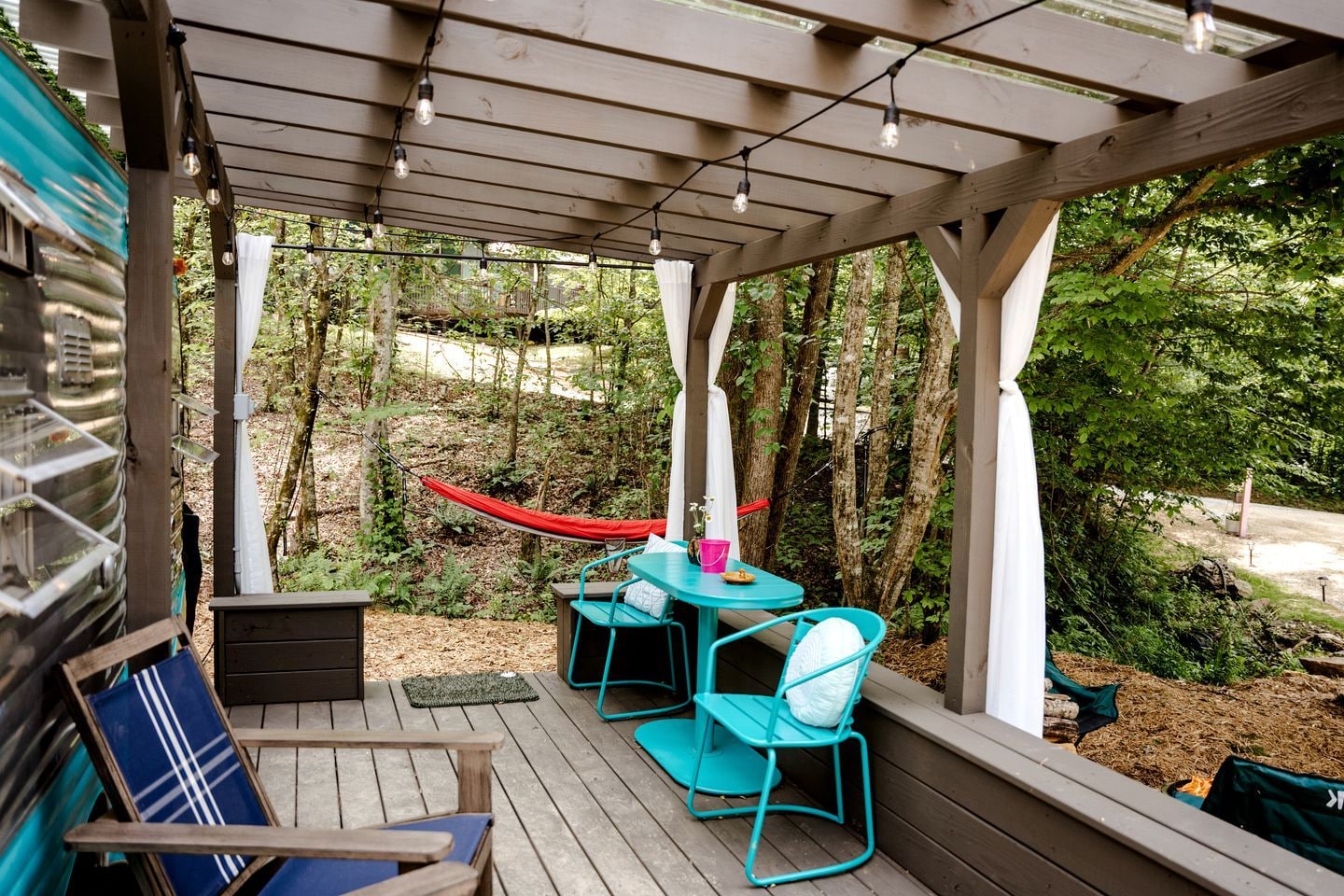 A covered outdoor area with a table and chairs, a hammock, and a view of the surrounding forest.