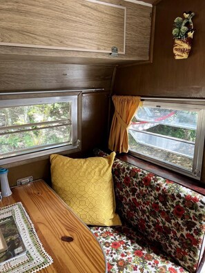 Ein gemütliches Wohnmobil-Interieur mit Holztisch, gelbem Sitzkissen und einer floral gemusterten Couch.
