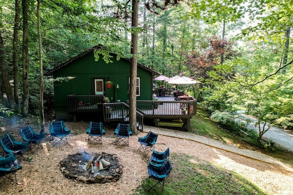 A green cabin with a deck, outdoor seating, and a fire pit.