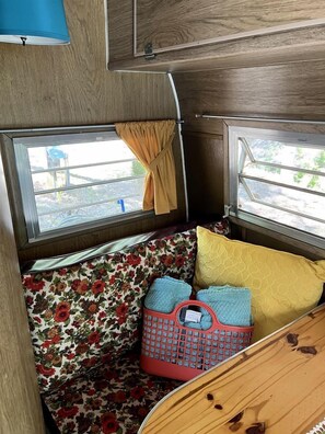 A campervan interior with a floral-patterned bench, a red basket, and two windows with curtains.